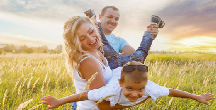 Parents smiling and holding child while standing in a field